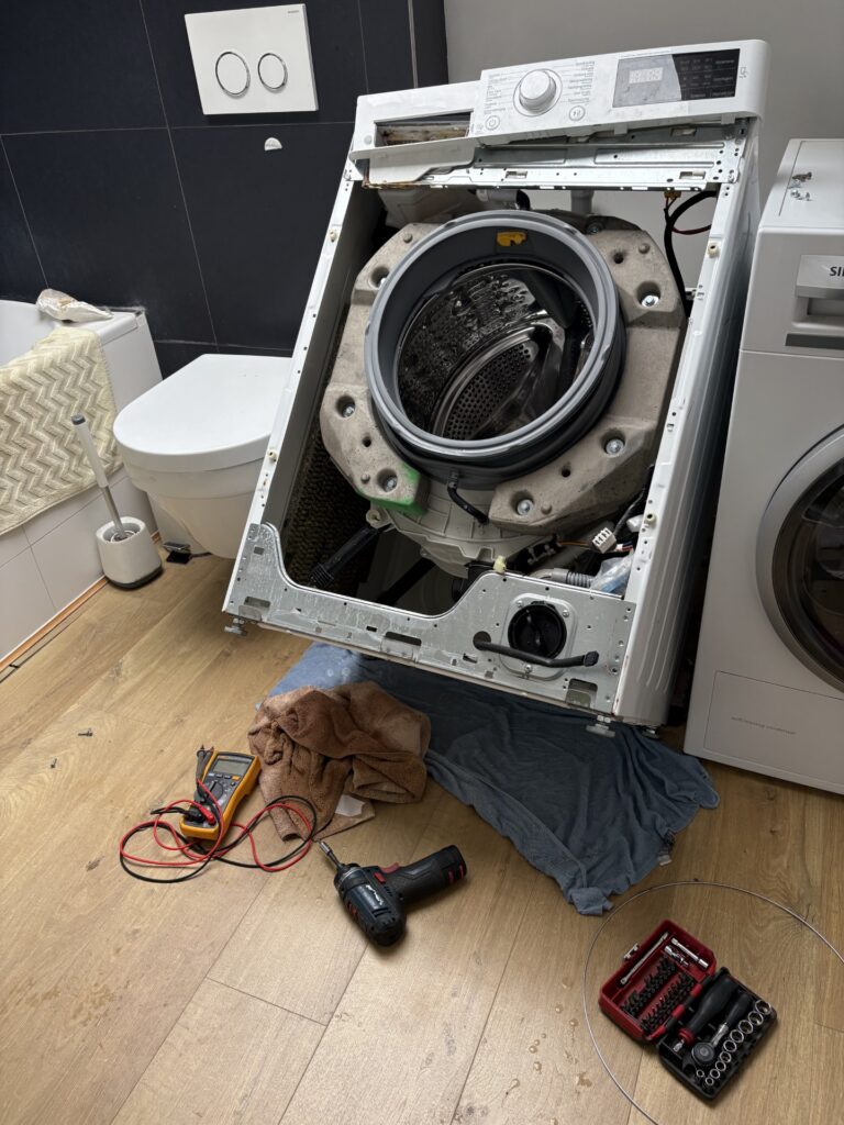 Lave-linge ouvert pendant une réparation à domicile, avec les outils du technicien au sol